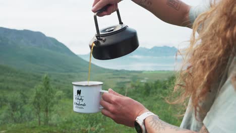 Woman-Pouring-Out-Coffee-From-A-Kettle-Into-A-Cup-Outdoors---close-up