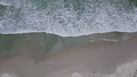 Calm-scene-with-ocean-waves-washing-onto-a-sandy-beach-from-above