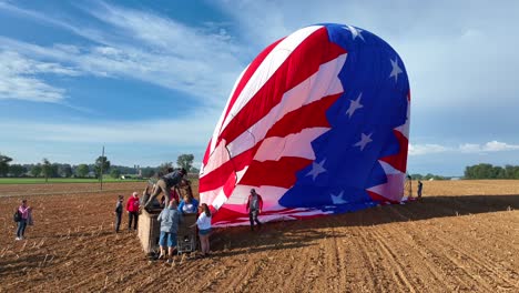 Group-of-people-landing-with-hot-air-balloon-on-rural-farm-field-during-sunny-day-and-leaving-basket