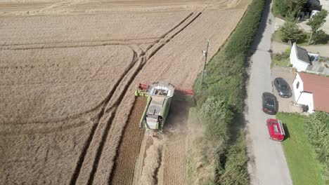 Aerial-footage-of-a-combine-harvester-harvesting-a-wheat-crop-next-to-homes