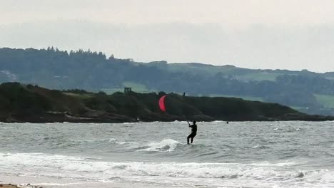 Kiteboarding-surfers-riding-extreme-windy-coastal-waves-near-Wales-stormy-overcast-beach
