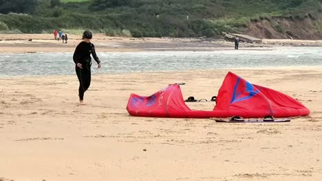 Active-kitesurfing-couple-preparing-water-sports-equipment-on-windy-overcast-beach-in-Wales