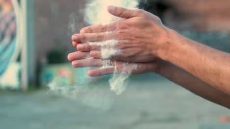 Claps-hands-covered-in-powder,-creating-a-burst-of-flying-particles