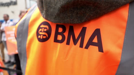 A-striking-doctor-wears-an-orange-British-Medical-Association-tabard-on-an-industrial-action-picket-line-at-in-slow-motion