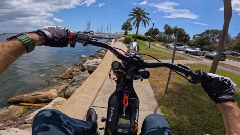 Man-on-Ebike-performing-stunts-near-a-water-body,-FPV-of-man-doing-wheelies-on-the-sidewalk