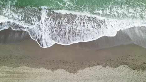 Top-down-aerial-view-of-waves-crashing-on-sandy-beach