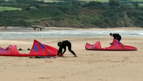 Active-kitesurfing-couple-preparing-freestyle-water-sports-equipment-on-stormy-overcast-beach-in-Wales