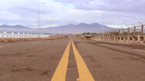 A-wide-angle-road-with-a-yellow-line-and-people-cycling-in-the-background