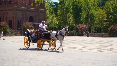 4k-Video-of-Tourists-ride-on-the-horse-and-carriages-while-visiting-The-Plaza-de-España-in-the-Parque-de-María-Luisa,-southern-Spain