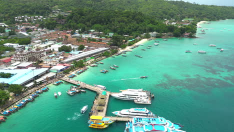 Koh-Phi-Phi-island-harbor-with-moored-boats-and-docked-ferries,-aerial-tilting-upward