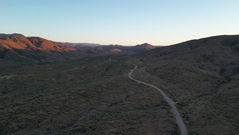 Camino-Vacío-Del-Desierto-En-Medio-De-Un-Vasto-Valle-Desértico-Con-Montañas-Iluminadas-Por-El-Amanecer-De-La-Mañana