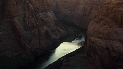 Handheld-shot-of-the-large-calm-Colorado-river-surrounded-by-huge-orange-sandstone-rock-cliffs-caused-by-erosion-near-Page,-Arizona-during-a-desert-evening-in-spring-at-dusk