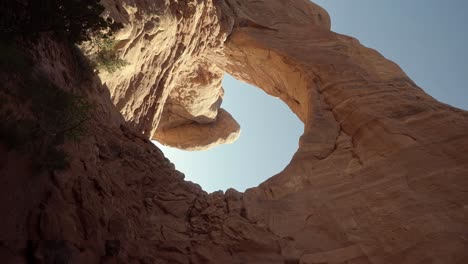 Pan-right-vertical-handheld-wide-landscape-shot-of-large-stunning-natural-orange-sandstone-arch-formations-with-sun-shining-through-them-on-a-hike-in-southern-Utah-on-a-sunny-warm-spring-morning