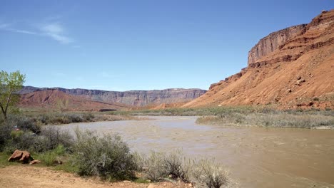 Pan-left-wide-landscape-shot-of-a-stunning-orange-sandstone-rock-mountain-peak-with-the-Colorado-river-below-near-Moab,-Utah-on-a-warm-sunny-spring-morning