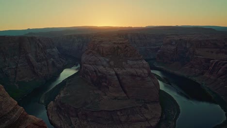 Extreme-wide-tilt-up-landscape-shot-revealing-the-famous-Horseshoe-bend-colorful-sandstone-rock-formation-formed-from-the-Colorado-river-near-Page,-Arizona-during-a-sunny-spring-desert-sunset-at-dusk
