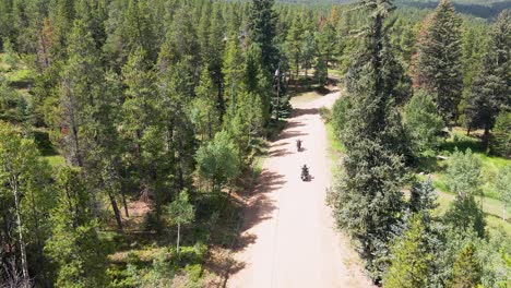 Aerial-view-over-the-treetops-of-a-dirt-road-with-two-motorcycles-driving-along-the-curves