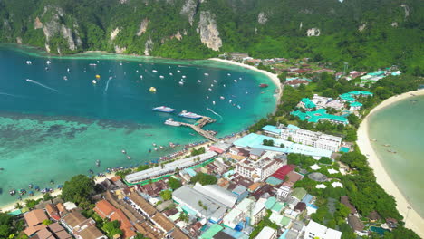 Koh-Phi-Phi-island-harbor-surrounded-by-tourist-boats,-passenger-ferries,-and-hotels,-aerial-shot