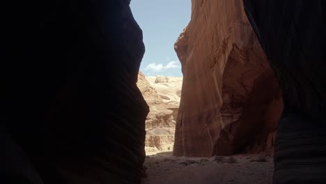 Tilt-down-handheld-wide-shot-revealing-a-large-opening-from-a-hike-through-a-tall-orange-sandstone-slot-canyon-in-buckskin-gulch-in-southern-Utah-near-Arizona-on-a-warm-sunny-spring-morning