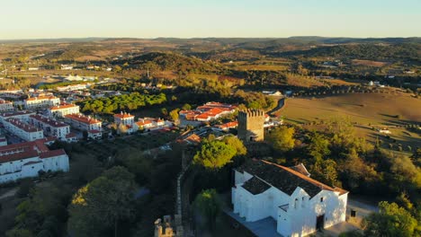 Toma-De-Drone-De-Un-Edificio-De-Capilla-Blanca-En-Una-Colina-Con-Muralla-Medieval-Y-Torre-En-Alentejo,-Portugal