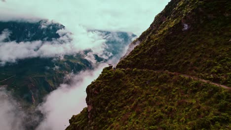 Lateral-drone-flight-along-trekking-path-with-post-rain-clouds,-lush-green-landscape,-and-scenic-rest-area