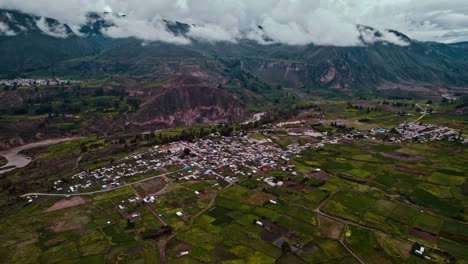 Aerial-drone-panorama-of-Maca-district,-with-cloudy-skies,-revealing-the-Colca-River-and-the-village-of-Lari-in-the-background
