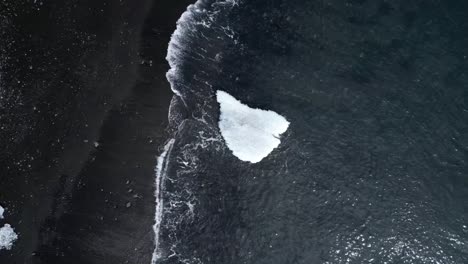 Diamond-beach-from-aerial-view-focusing-on-the-sea-waves-moving-towards-a-huge-iceberg-in-the-beautiful-black-sands-of-this-landscape