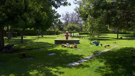 Low-aerial-dolly-shot-flying-over-flowered-gravesites-towards-a-decorative-fountain-at-a-mortuary-in-California