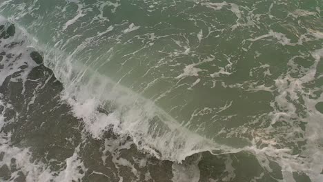 Smooth-cinematic-overhead-aerial-of-waves-crashing-in-shallow-water-on-to-a-pebble-beach