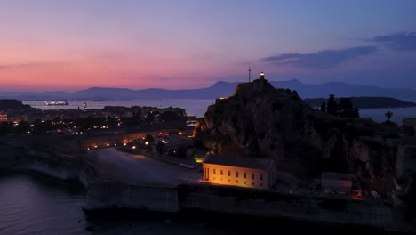 Night-aerial-view-over-Corfu-old-fortress-with-beautiful-colored-sky,-revealing-sailing-boats-and-coast-area