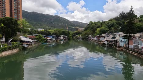 Pan-Left-View-Across-Calm-Waterway-Surrounded-By-Village-Buildings-In-Hong-Kong