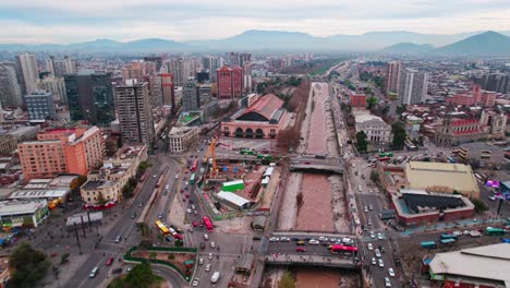 Aerial-view-establishing-over-the-Mapocho-river-and-the-cultural-center-Mapocho-station,-construction-site-and-high-flow-of-people,-mountains-with-pollution-in-the-background-Santiago-Chile