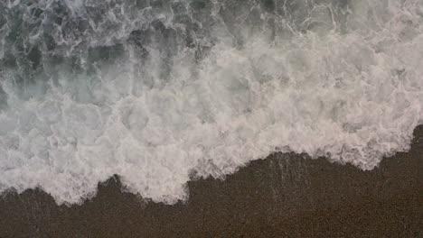 Gentle-crashing-waves-spread-whitewash-foam-across-pebble-beach,-real-time