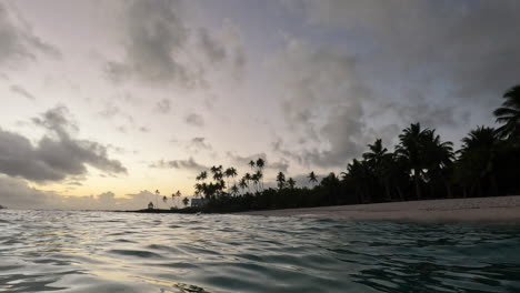 The-sun-sets-over-the-ocean-and-a-white-sandy-beach-with-palm-trees-along-the-coastline-in-Samoa