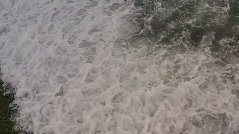 Whitewash-crashing-wave-spreads-and-drains-on-pebbles-at-beach-as-water-recedes,-slow-motion