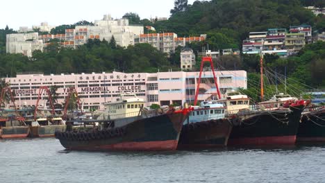 Segeln-Sie-An-Festgemachten-Fischereifahrzeugen-Im-Yachthafen-Der-Insel-Cheung-Chau-Vorbei,-Mit-Blick-Auf-Das-Buddhistische-Wai-Yan-Memorial-College-Im-Hintergrund