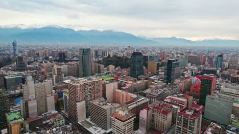 Dolly-in-establishing-aerial-view-of-downtown-Santiago-Chile-with-residential-and-government-buildings-with-the-Santa-Lucia-hill-in-the-center-and-the-cloudy-Andes-mountain-range-in-the-background