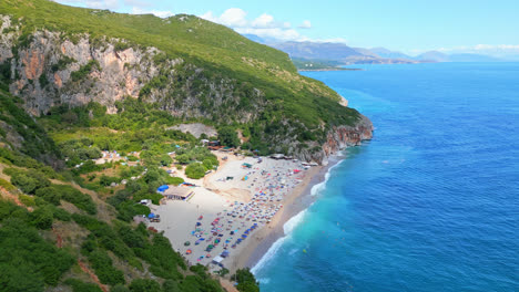 Aerial-drone-zoom-in-shot-of-tourists-sunbathing-along-the-Gjipe-Beach-in-Albania-with-waves-crashing-along-the-beachside