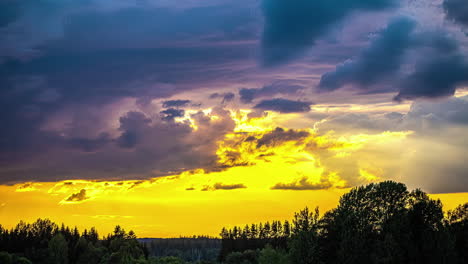 Timelapse-shot-of-dark-rain-clouds-over-a-serene-coniferous-forest-with-yellow-sky-after-sunset-in-the-background-during-evening-time