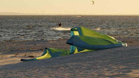 Yellow-kitesurfing-kite-lying-on-beach,-flapping-in-strong-wind-during-sunset-goldenhour