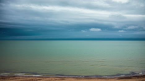 Timelapse-shot-of-dark-cloud-movement-over-sea-shore-with-waves-crashing-along-on-a-rainy-day