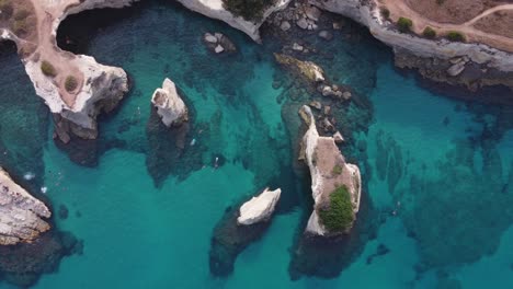Beautiful-rock-formation-in-the-mediteran-sea-with-people-taking-a-swimm-from-above