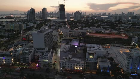 South-beach-ocean-drive-drone-establish-at-dusk,-sunset-skyline-and-clouds-background