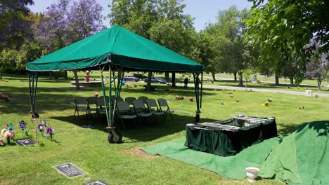 Slow-dolly-aerial-shot-of-a-burial-site-ready-for-interment-as-the-funeral-party-arrives-in-the-background-at-a-California-mortuary