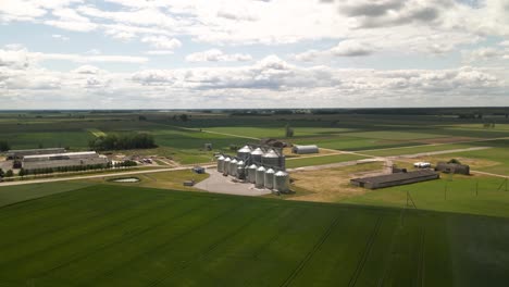 drone-view-of-agro-silos-granary-manufacturing-plant-storage-of-agricultural-products-and-grain-elevators-in-the-middle-of-a-green-cultivated-field,-zoom-in