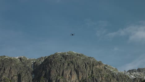 La-Silueta-De-Un-Drone-Filma-La-Cima-De-Una-Montaña-Contra-El-Cielo-Azul.