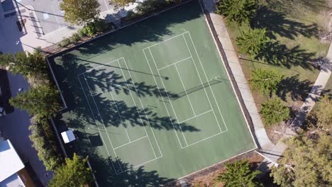 Rotierende-Luftaufnahme-über-Zwei-Von-Bäumen-Umgebene-Tennisplätze