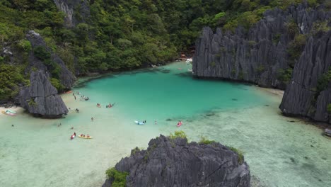 Aerial-jib-shot-of-Cadlao-Lagoon-or-Ubugon-Cove-in-El-Nido,-philippines-with-people-kayaking-and-swimming-in-Tropical-turquoise-water