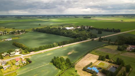 Aerial-shot-of-green-cultivated-fields-and-farmlands-besides-the-road-on-cloudy-summer's-day-in-Lithuania