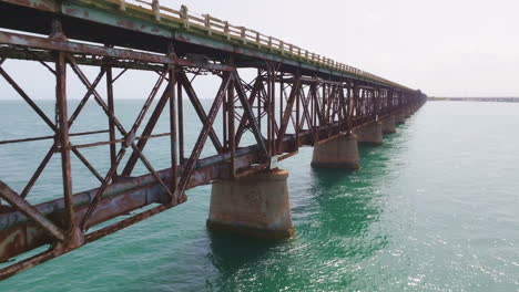Old-rusted-metal-support-beams-hold-up-bridge-and-piping-across-ocean-on-concrete-stilt-supports
