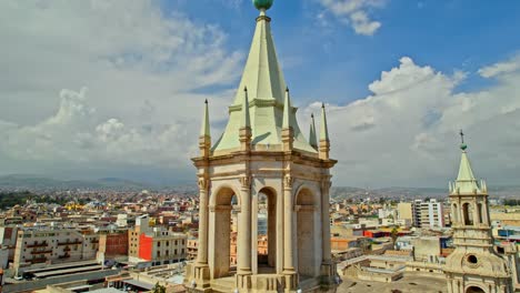 Drone-shot-descends-from-the-left-tower-of-Arequipa-Cathedral,-with-distant-clouds-and-the-small-left-tower-in-view